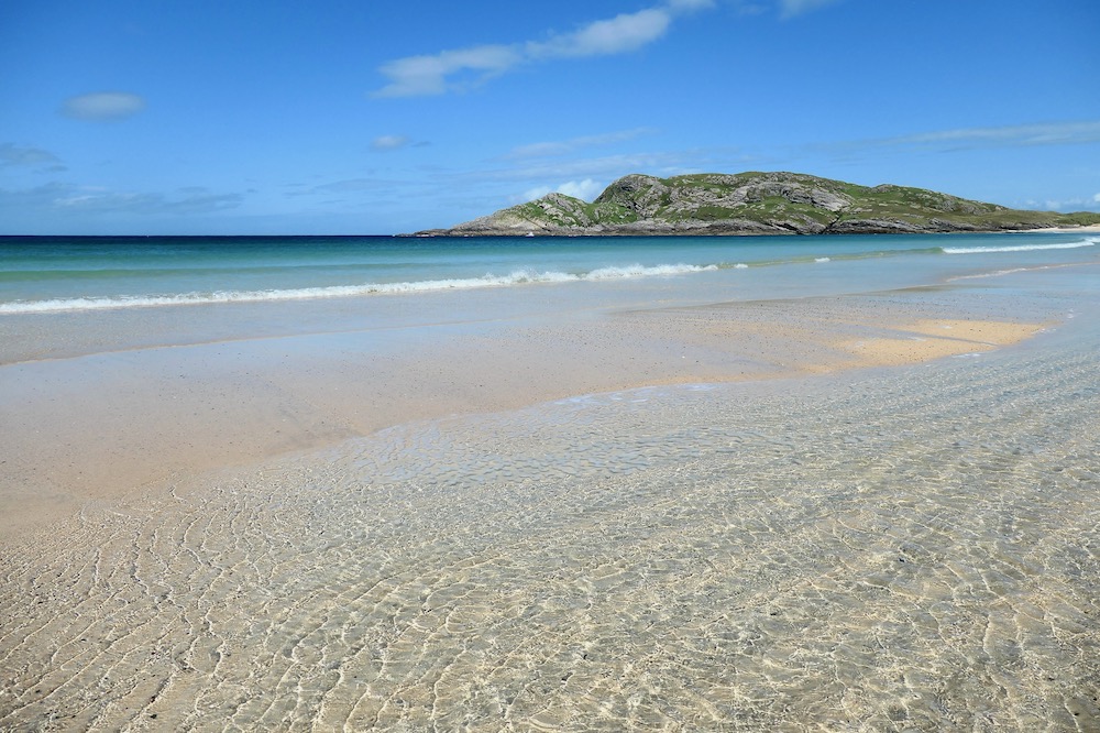 A stunning beach with rippled sand in the foreground, turquoise seas and a clear blue sky